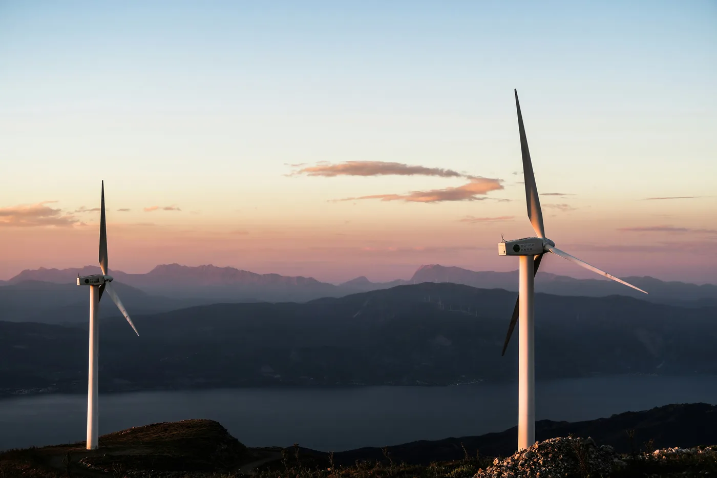Two wind turbines above a lake at sunset